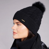 Woman wearing a black knit beanie with a fur pom-pom on a grey background