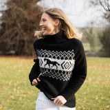 Woman wears a black sweater with a white pattern and white jeans in an outdoor setting