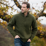 Man wearing a green sweater standing outdoors with trees in the background