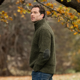 Man wearing a green knitted sweater standing outdoors with trees in the background