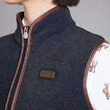 Close-up of a navy blue gilet with brown trim and a brand logo, worn by a person.