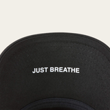 Under rim of black baseball cap with 'Just Breathe' in white writing on white background