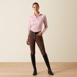 Woman wears a pink long sleeve top and brown riding leggings on a beige background