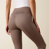 Woman wears a pair of brown riding tights and a white top on a beige background