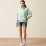 Woman wearing a light green jacket and denim shorts on a plain background