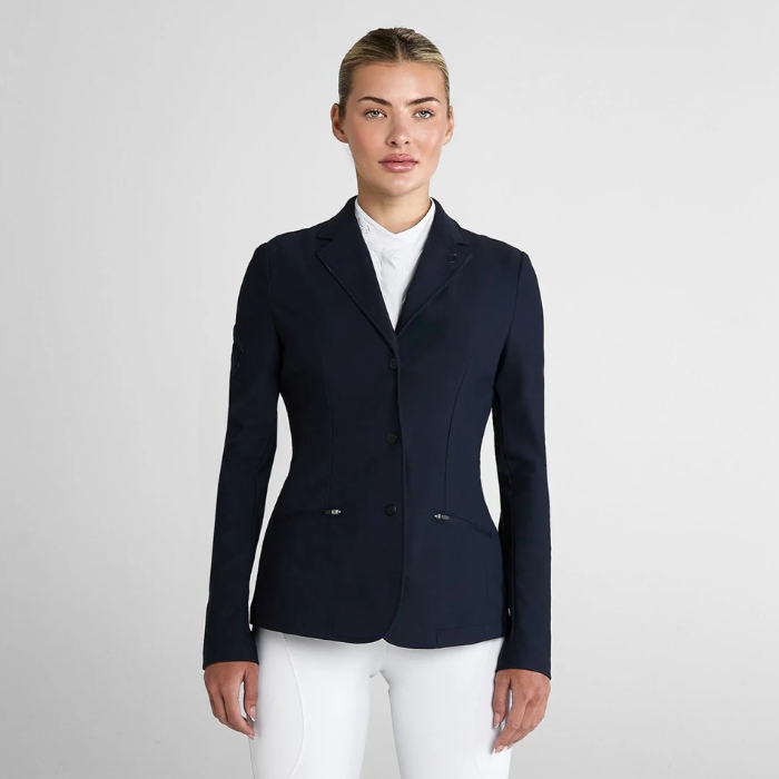 Woman wearing a smart navy jacket and white breeches on a light grey background