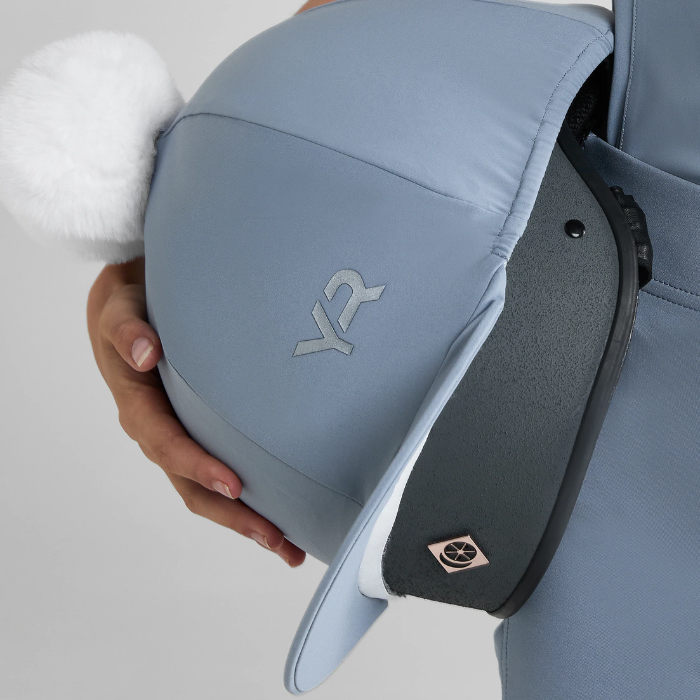 Close-up of a riding hat with a blue cover and visible brand logo on a light grey background