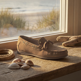 Brown loafers on a wooden surface with a beach view through a window.