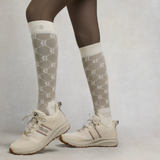 Person wears long riding socks with beige trainers on a grey background