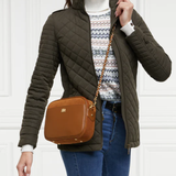 Person wearing a green quilted jacket with a brown crossbody bag against a white background