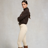 Woman wearing a brown sweater and beige jeans against a plain background