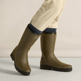 Brown-green rubber boots worn with beige trousers on a light background