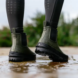 Person wearing green rubber boots standing in water with a blurred natural background