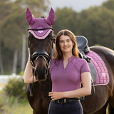 Woman in a pink shirt standing next to a horse wearing pink ear protectors.