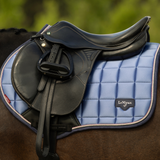 Black horse saddle with blue glossy pad underneath worn by a dark coloured horse