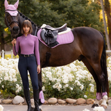 Woman in equestrian attire standing next to a horse with a pink bridle and saddle pad in a floral setting.