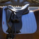 Saddle on a horse with a blue saddle pad, blurred background