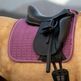 Black saddle on a horse with a pink saddle pad against a blurred natural background