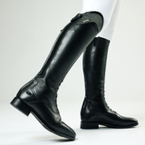 Black riding boots worn with white leggings on a light grey background