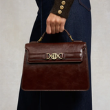 Brown leather handbag with gold clasp held by a person wearing a dark coat.