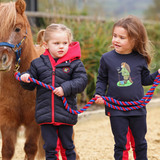 two young children lead a pony wearing navy blue long sleeve t-shirt with cartoon pony motif.