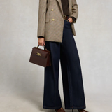 Person wearing a plaid blazer, dark trousers, and holding a brown handbag against a plain background