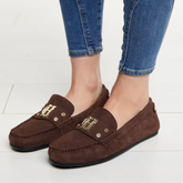 Brown loafers with gold accents worn with blue jeans on a white background