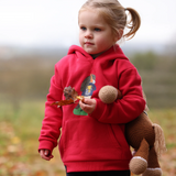Small girl wearing a red hoeded sweatshirt holds toy pony and leaf with blurred outdoor background