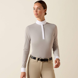 Woman wearing a light grey equestrian shirt with white collar and beige breeches on a beige background