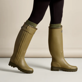 Person wears a pair of green wellington boots and black leggings against a neutral background