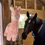 Pink plush llama toy hanging in a stable with a horse in the background