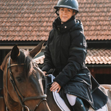 Woman on a horse wearing a black coat with a roof in the background