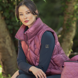 Woman wearing a pink puffer gilet sitting outdoors with greenery in the background