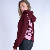 Person wearing a burgundy hoodie with pink logo on a white background