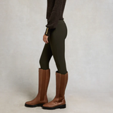 Person wearing green riding leggings and brown knee-high boots on a plain background