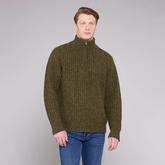 Man wearing a green knitted sweater and blue jeans against a grey background