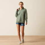 Woman wearing a green sweatshirt and denim shorts on a beige background
