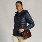 Woman wearing a navy puffer jacket holding a brown leather bag against a neutral background