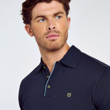 Man wearing a navy polo shirt with a small logo on a light grey background