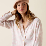 Woman wears a white and pink linen shirt and a beret on a plain background
