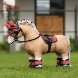 Plush toy horse with a red bridle and saddle on grass