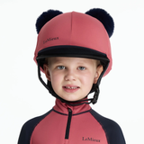 Child wearing a red equestrian helmet with black pom-poms and matching outfit on a white background