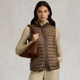 Woman wearing a brown puffer gilet holding a brown bag against a neutral background