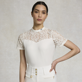 Woman wears a white top with lace collar on a grey background