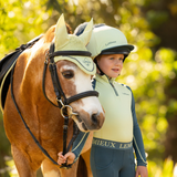 Child in equestrian gear standing next to a horse with a blurred green background