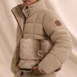 Person wears a natural borg material jacket clutching a faux fur back on a beige background