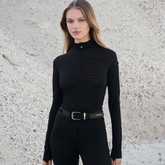 Woman wearing a black houndstooth outfit with a belt against a textured wall.
