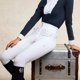 Person wearing equestrian attire sitting on a vintage suitcase.
