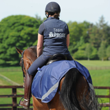 Horse wearing a blue exercise sheet and rider wears a blue gilet with TEAM BUCAS embroidery in an outdoor setting