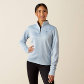 Woman wearing a light blue pullover with a logo on a beige background